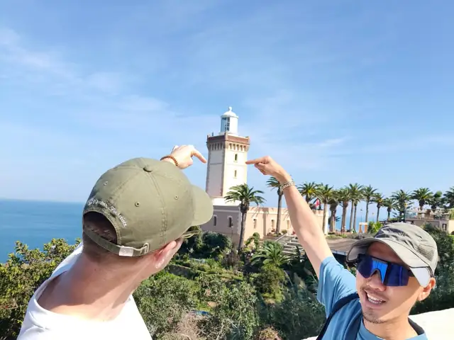 Two travellers framing the Cap Spartel lighthouse with their fingers
